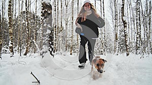 A girl and her Jack Russell Terrier dog are running through the woods.