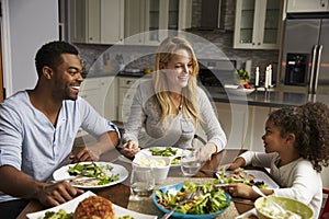 Girl and her mixed race parents dining in their kitchen