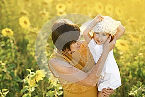 Girl in her mom`s arms laughs merrily while wearing big hat.