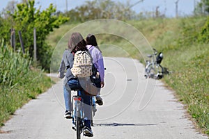 girl and her mother with backpacks on their shoulders riding their bicycles leisurely on a country bike path photo