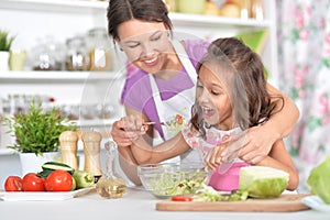 Girl with her mother cooking salad together at kitchen