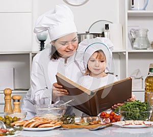Girl and her mother are looking new recipe in big book in the kitchen