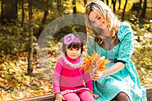 Girl and her mother playing outdoors with autumnal maple leaves. Baby girl picking golden leaves