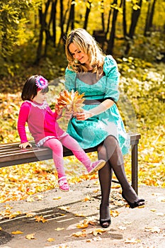 Girl and her mother playing outdoors with autumnal maple leaves. Baby girl picking golden leaves