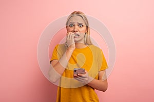 Girl with her smartphone. Scared and afraid expression. Pink background