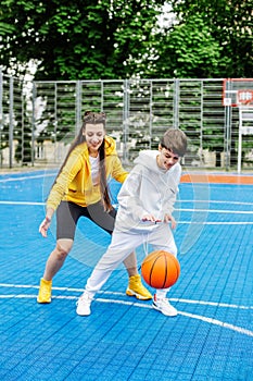 Girl and her younger brother, teenager, play basketball on modern basketball court under open sky