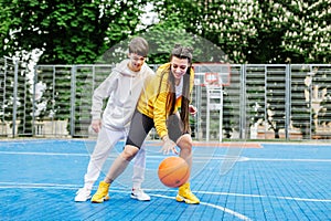 Girl and her younger brother, teenager, play basketball on modern basketball court under open sky