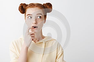 Girl hesitates while having idea in her mind. Portrait of nervous attractive ginger woman with two buns hairstyle