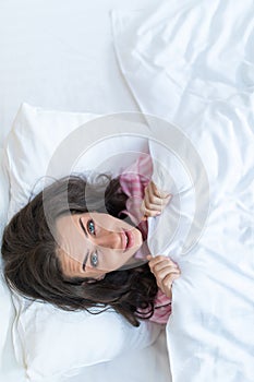 Girl hides her face in bed. Cheerful girl in bed hiding her face under the blanket. Teenage girl lying under a blanket. Woman