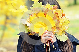 Girl hides her face behind yellow autumn leaves, bouquet, autumn