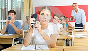 Girl high school student using mobile phone on lecture in class