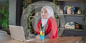 Girl with hijab typing on laptop and relaxing