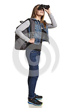 Girl hiker with backpack looking through binoculars