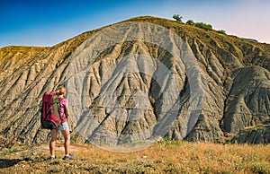 Girl hiker with backpack standing against badland photo