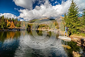 Girl hiker posing on the rock in the mountain lake in autumn colors