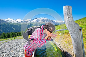 Girl hiker quenches thirst at the fountain during a mountain trekking