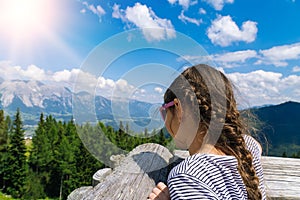 Girl hiking on beautiful summer day in alps mountains Austria, resting on rock and admire amazing view to mountain peaks