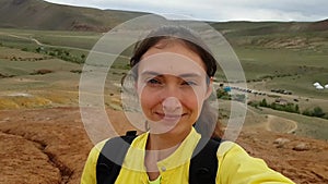 Girl hitchhiker brunette with a backpack makes a selfie against red mountains of Kyzyl Chin Altai Mars.