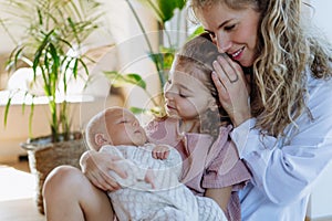 Girl hodling little baby, mother looking. Big sister meeting newborn baby syster, enjoying together time.