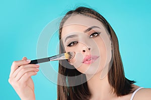 Girl hold blush blusher apply powder visage isolated over studio background. Young woman powdering cheeks. Makeup brush