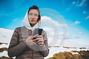 Girl hold in hands mobile phone, tourist planning trip in snow mountain on blue sky background, person type message on smartphone