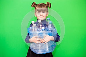 Girl hold trash bag and plastic bottle and shows interest in environmental issues  on green background. Child accustomed