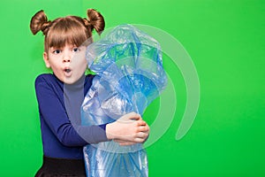 Girl hold trash bag and plastic bottle and shows interest in environmental issues isolated on green background. Child accustomed