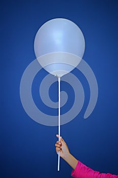 A girl hold a white ballon in front of a blue colour background