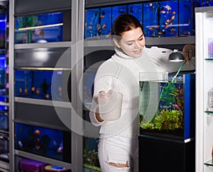 Girl holding aquarian net and water container next to aquarium w