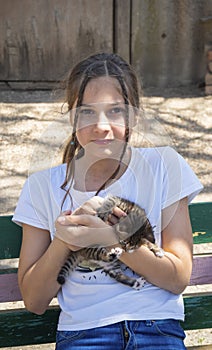 A girl is holding a baby cat in her arms. Children and pets. A teenage girl hugs a cute little kitten sitting on a wooden bench. A