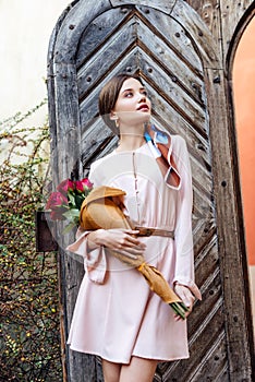 Girl holding bouquet of red roses while standing near old wooden door and looking away