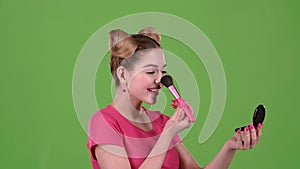 Girl holding a brush in her hand and powdering her face. Green screen. Close up. Slow motion