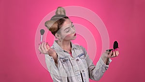 Girl holding a brush in her hand and powdering her face. Pink background