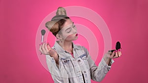 Girl holding a brush in her hand and powdering her face. Pink background. Slow motion