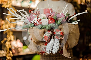 Girl holding a christmas composition with pink orchids, white roses, fir-tree branches, red apple and candle in the