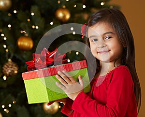 Girl Holding Christmas Present In Front Of Tree