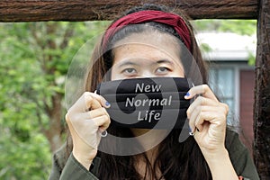 A girl holding and covering her face with black cloth mask written - New Normal Life.