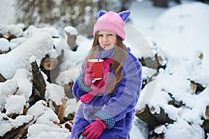 girl holding cup of hot drink and sitting on grass. female hands holding hot chocolate with marshmallow in a red mug.