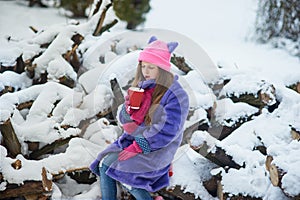 girl holding cup of hot drink and sitting on grass. female hands holding hot chocolate with marshmallow in a red mug.