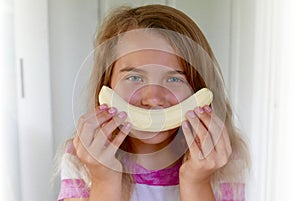 Girl holding a curved banana in front of her mouth to simulate a smile