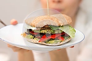 Girl holding delicious vegan burger on white plate in hand