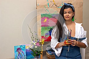 Girl holding dirty painting brushes in hands with picture on background. The artist finished the abstract painting