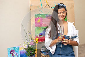 Girl holding dirty painting brushes in hands with picture on background. The artist finished the abstract painting