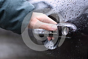 Girl holding the door handle of a wet car on a rainy day