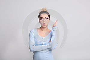 Girl holding finger up, having idea on grey background