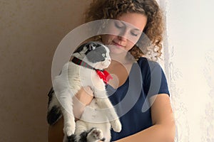 A girl is holding a fluffy cat in a scarf that looking out of the window