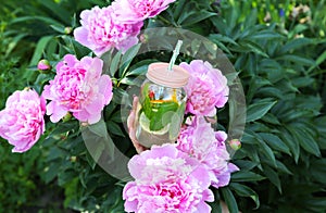 Girl holding fresh lemonade in jar with straw. Hipster summer drink in hand with peonies. Eco-friendly in the nature. Lemons,