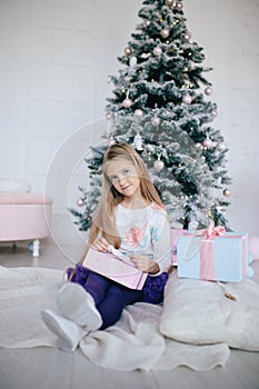 Girl holding a gift box near the Christmas tree. Kid opening Xmas present