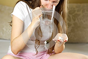 Girl holding a glass of water and pills. Closeup