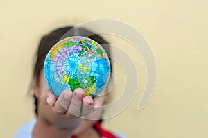 A girl is holding the globe by her hands with yellow background. The concept of saving the world or caring for the world